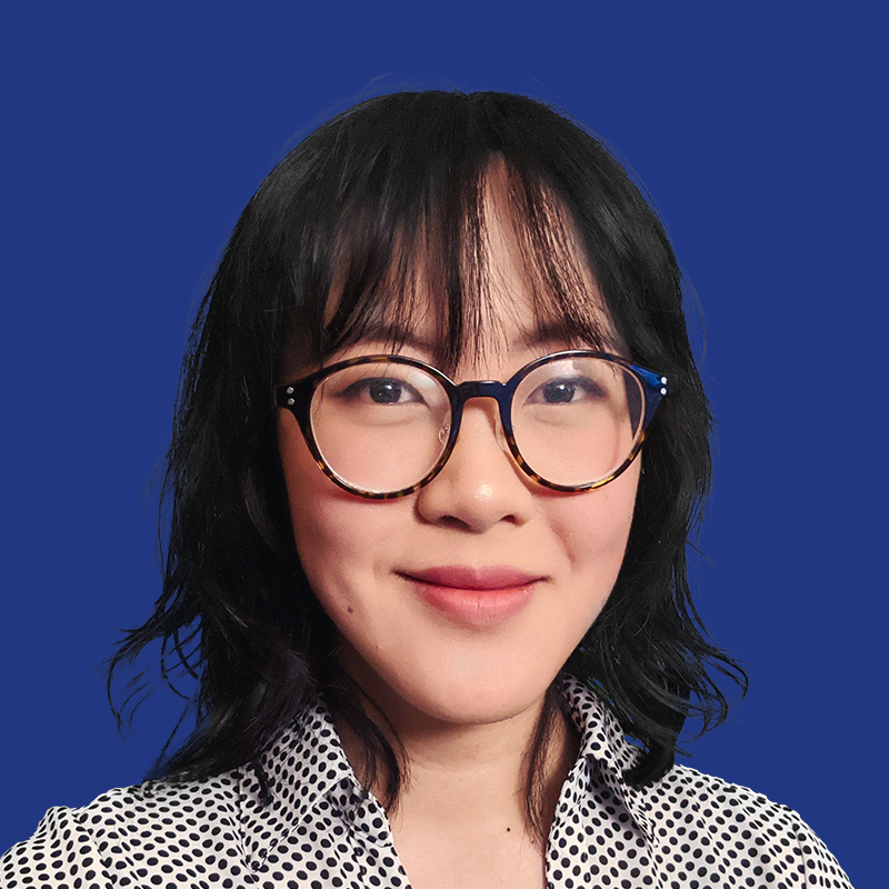 Headshot of Eileen Chi smiling, with shoulder length black hair, wearing glasses and a white polka dot blouse against a blue background